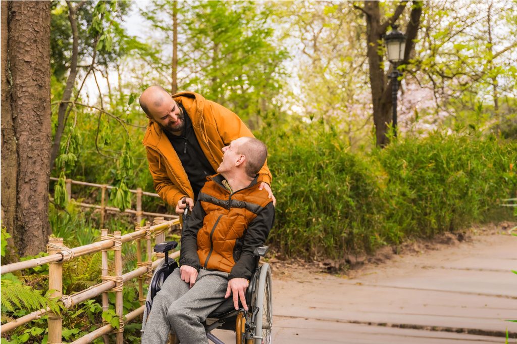 Behinderter Mann im Rollstuhl mit Begleitperson lachen sich an